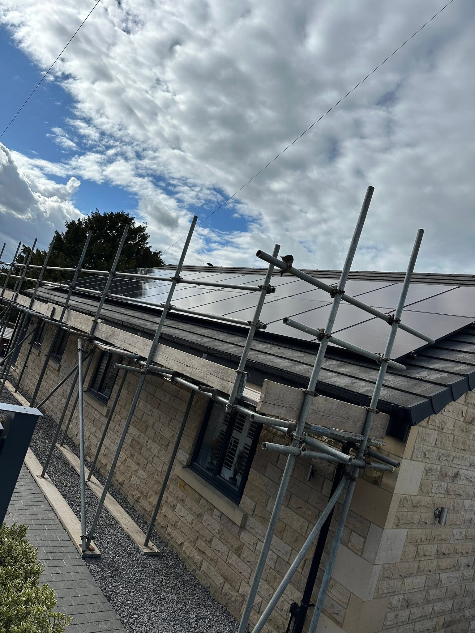 Solar panels being fitted to a stone house roof behind scaffolding