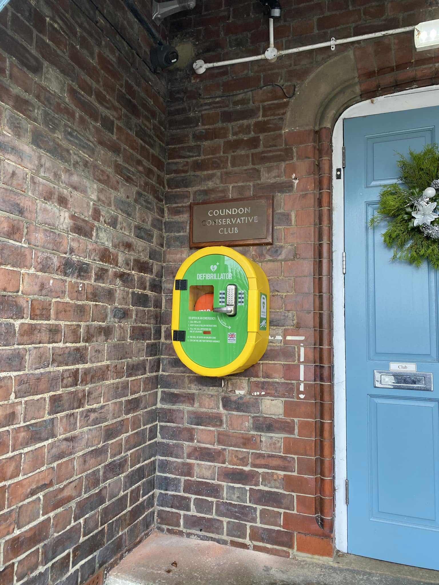 A defibrillator cabinet fitted on the brick wall beside the door of Coundon Conservative Club